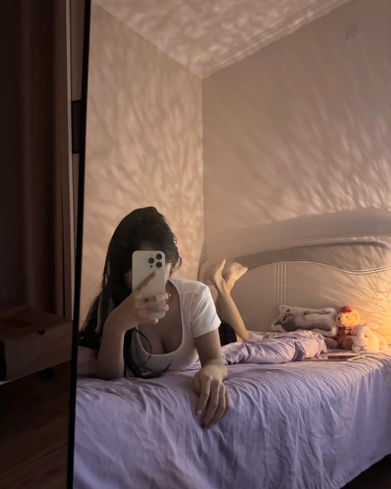 Cô gái dùng điện thoại che mặt khi nằm trên giường
