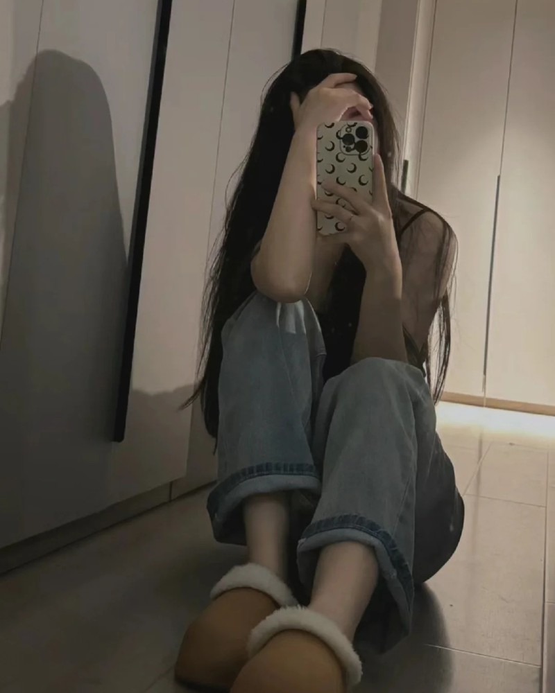 Cô gái ngồi dựa tường dùng điện thoại che mặt