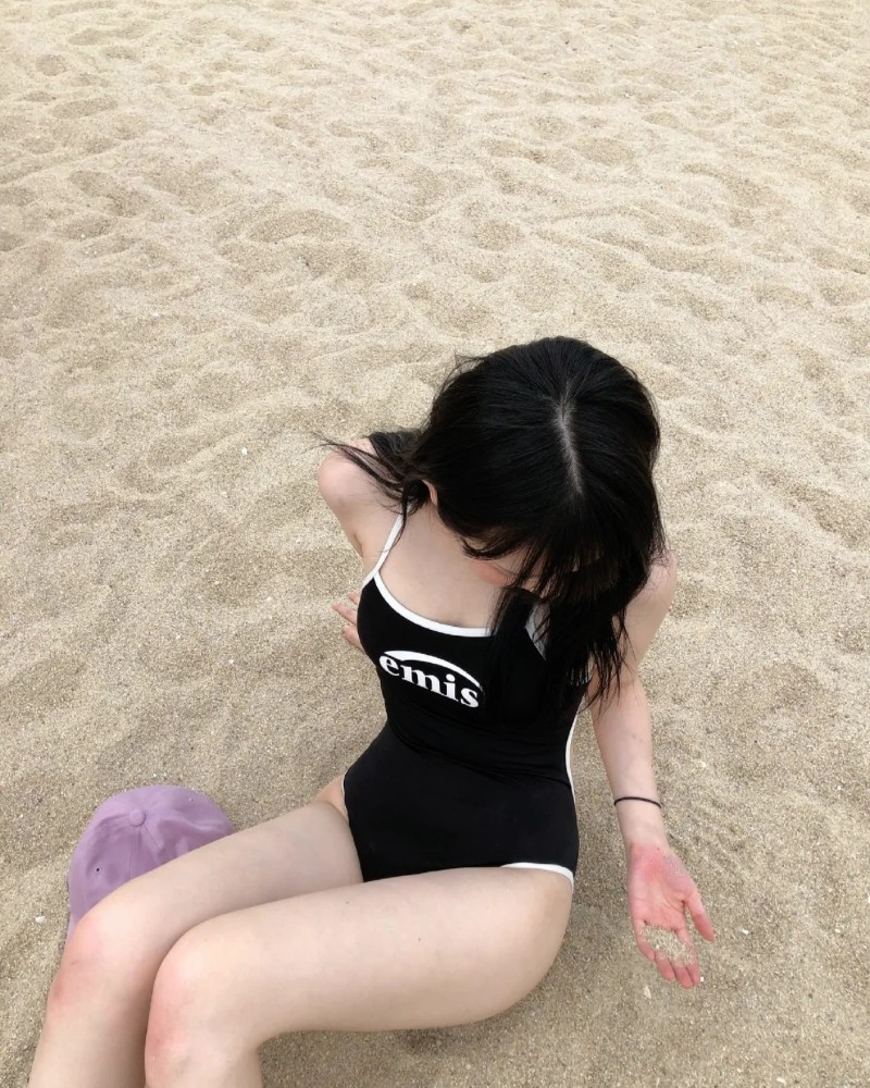 Cô gái ngồi thu mình trên bãi biển với áo tắm đen