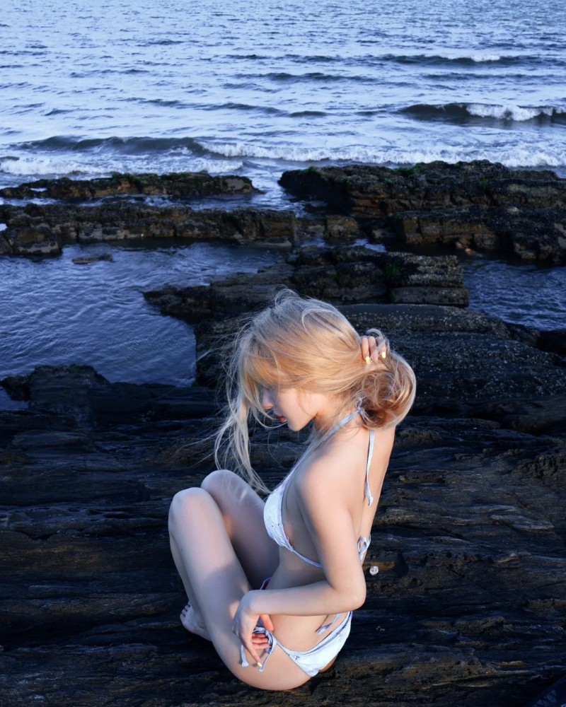 Cô gái ngồi dựa trên đá gần mặt biển
