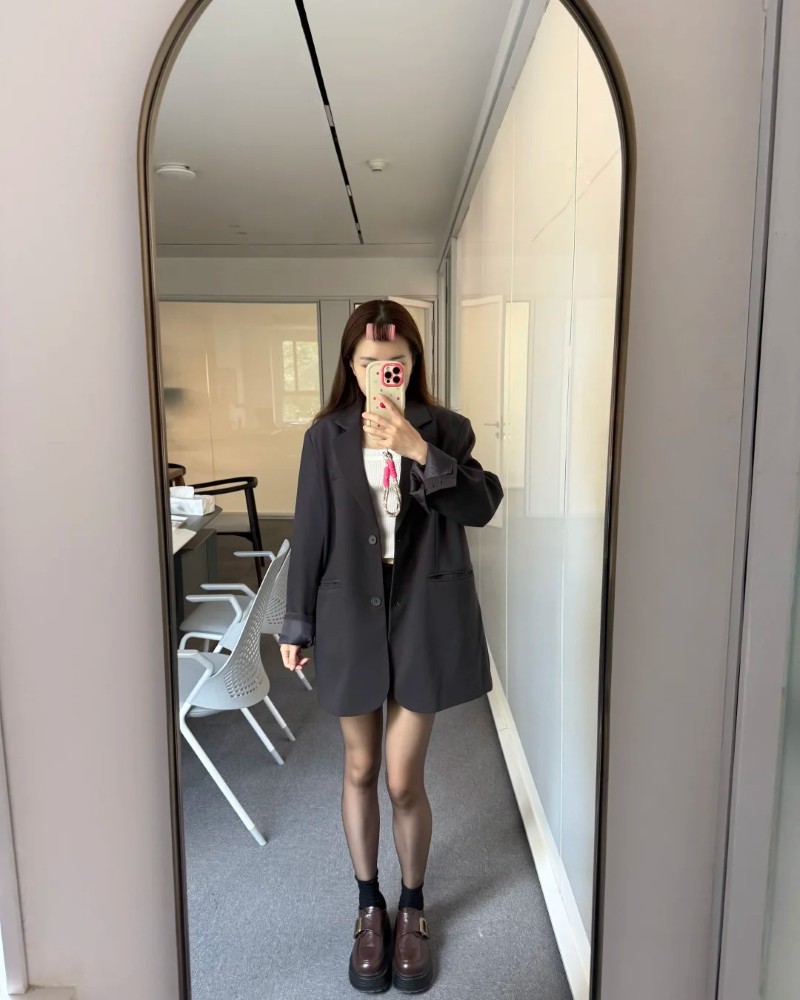 Người phụ nữ trẻ đứng trước gương với outfit đi làm