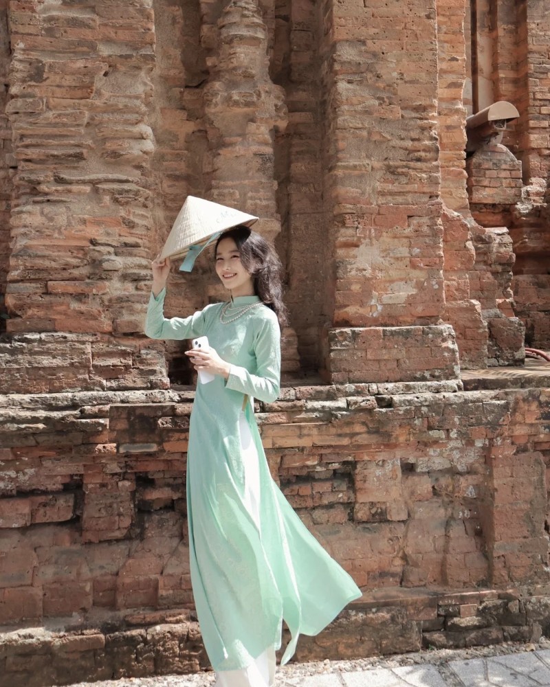 Cô gái mặc áo dài đứng trước bức tường gạch