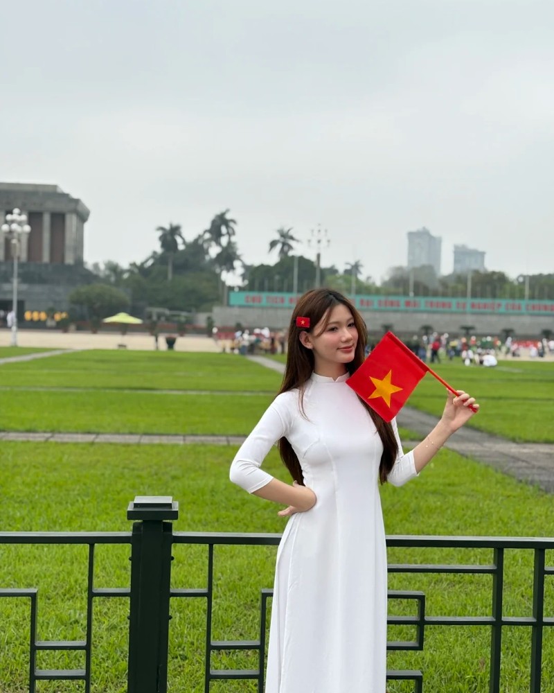 Người đẹp mặc áo dài trắng đứng trước bãi cỏ