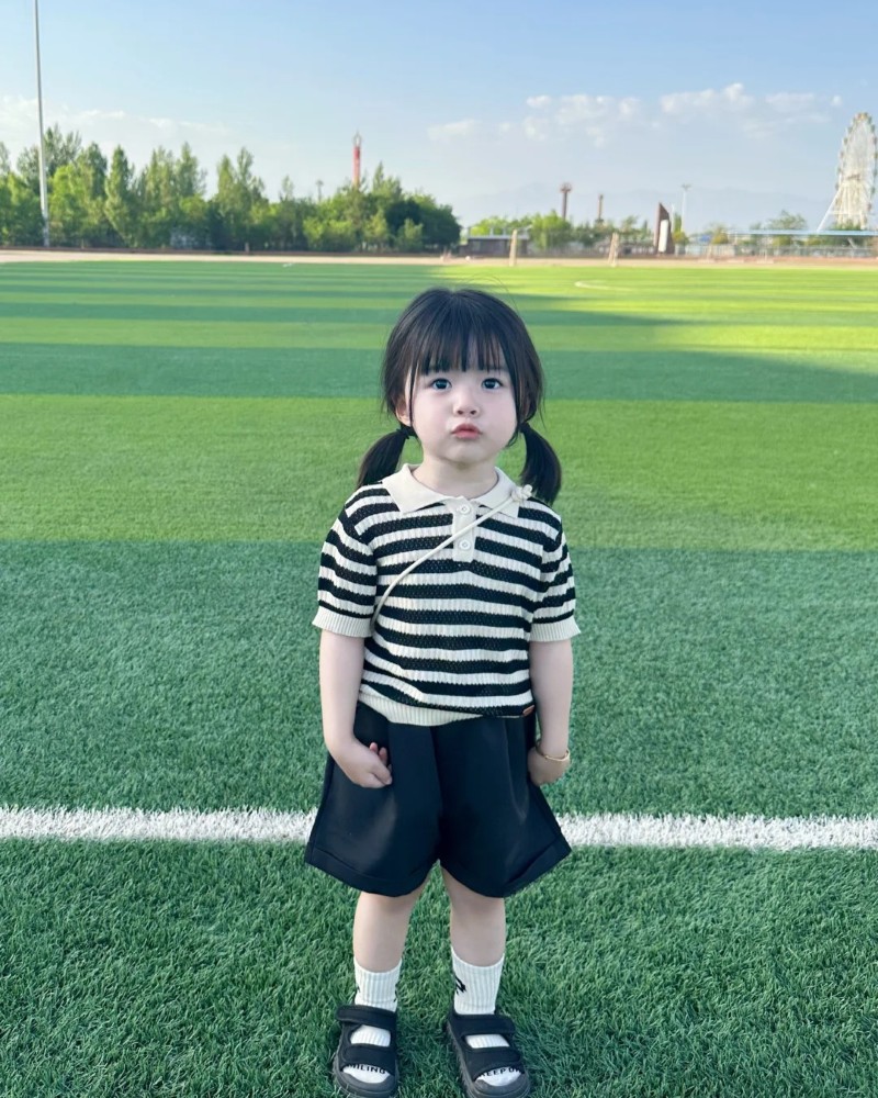 bé gái đứng trên sân cỏ tạo dáng vui vẻ